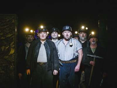 A group of miners stand together with their lights shining at the camera