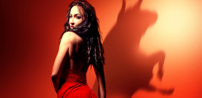 Side view of Carmen, looking over her shoulder at the audience. A silhouette of a bull shows on the red wall.