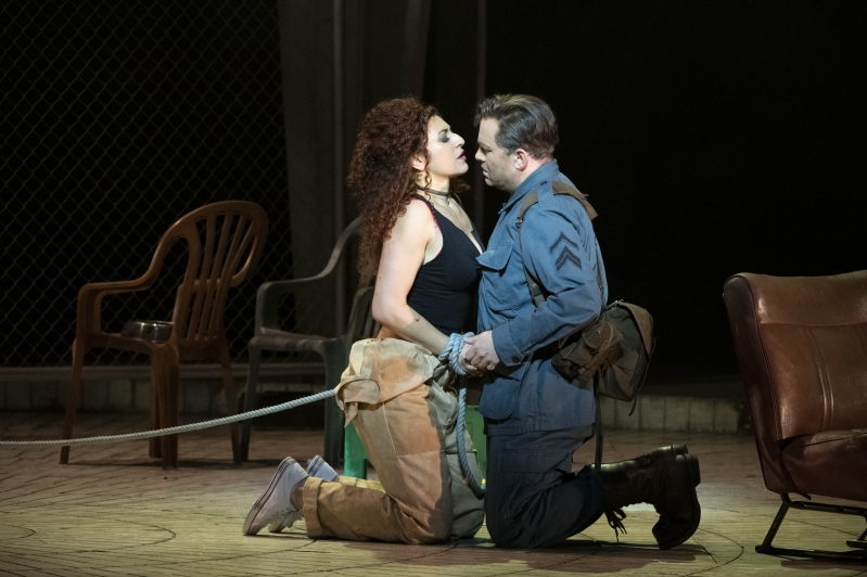 Soldier and woman kneeling on floor facing each other holding hands, woman has rope around her wrists.