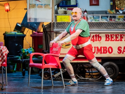 WNO Don Pasquale Andrew Shore Don Pasquale Photo credit Robert Workman 070 Robert Workman 2019 Man in tight red leotard and yellow glasses lunging against chair.