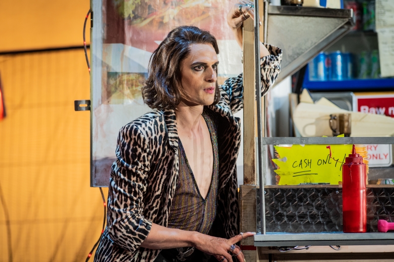 Man leaning against burger van in leopard print jacket.