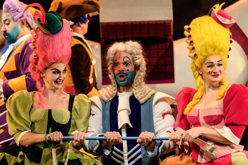 WNO La Cenerentola Aoife Miskelly Clorinda Giorgio Caoduro Dandini Heather Lowe Tisbe Photo credit © Jane Hobson 7623 Jane Hobson Clorinda and Tisbe, smiling, stand either side of Dandini, who appears surprised.