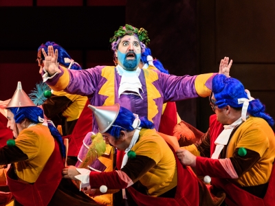 WNO La Cenerentola Fabio Capitanucci Don Magnifico WNO Chorus Photo credit © Jane Hobson 2001 Jane Hobson Don Magnifico appears shocked, his hands in the air. He is surrounded by the WNO Chorus, dressed in red, yellow and blue outfits.