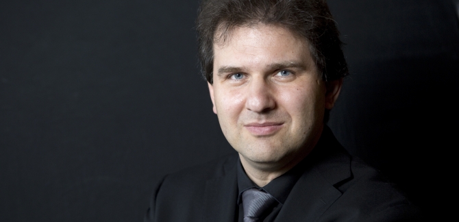 Close-up shot of Tomas Hanus in a suit and tie, on a grey background.