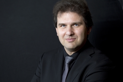 Close-up shot of Tomas Hanus in a suit and tie, on a grey background.