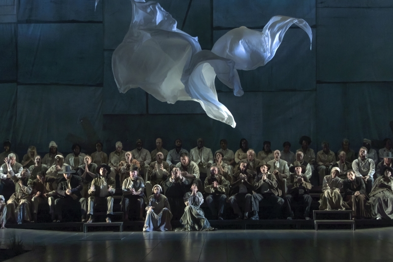 Group sit at the back of a stage, with a sail falling from the ceiling towards them