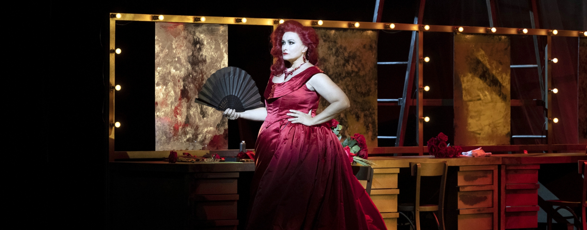 Woman in red dress stands before dressing mirrors and lights