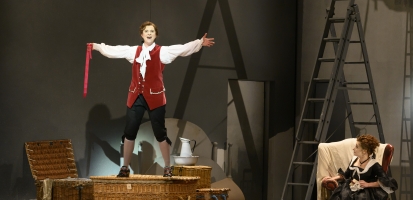 Man standing on box singing with arms outstretched. 