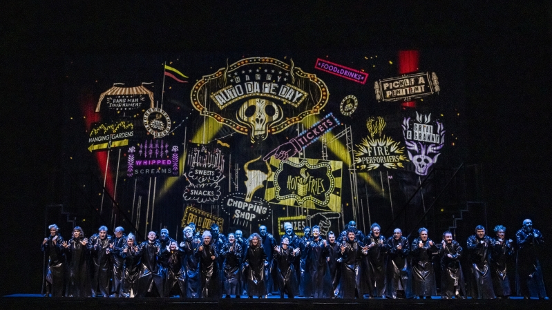 A group in long black coats stand before a display of colourful Spanish and Latin American inspired displays