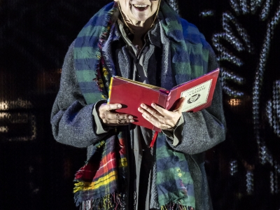 A woman with bright orange hair reads from a red book