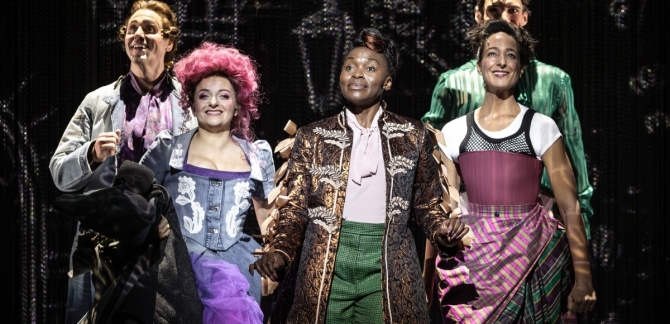 A close-up image of Candide, Cunégonde, the Narrator | Pangloss, Paquette and Maximilian standing in formation. The Narrator | Pangloss stands front and centre, and everyone smiles at the audience.