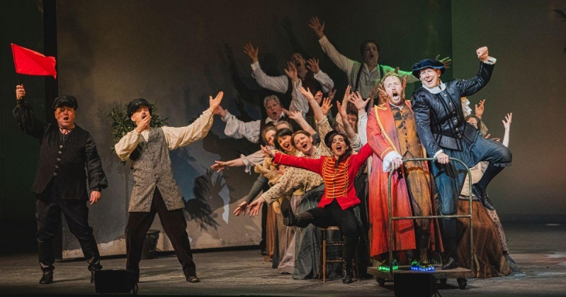 POL Blog 2 Photo 2 The cast of Play Opera LIVE sing the Italian song Funiculì, Funiculà. Most of them are pretending to be aboard a funicular railway train, and are excited with their hands up in the air. To the left are two men, one blowing a whistle and one holding a flag.